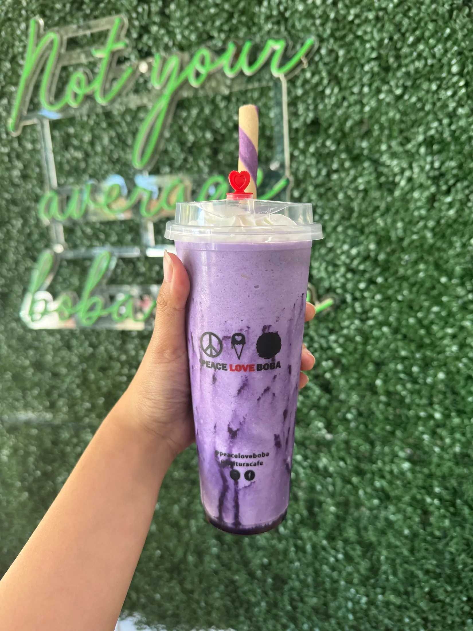 A purple ube boba drink in front of the neon sign